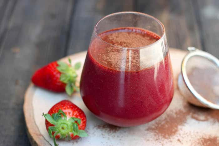 batido rojo de fresas dentro de un vaso de cristal encima de una tabla