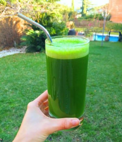 zumo verde en un vaso de cristal con pajita metálica, sostenido por una mano de mujer