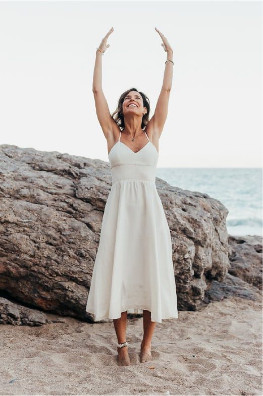 mujer con vestido blanco en la playa con los brazos hacia arriba