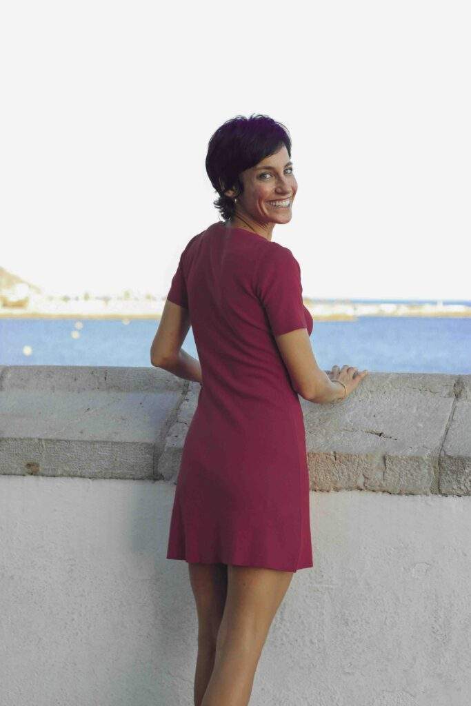 Mujer con vestido rojo en un muro con vistas al mar sonriendo