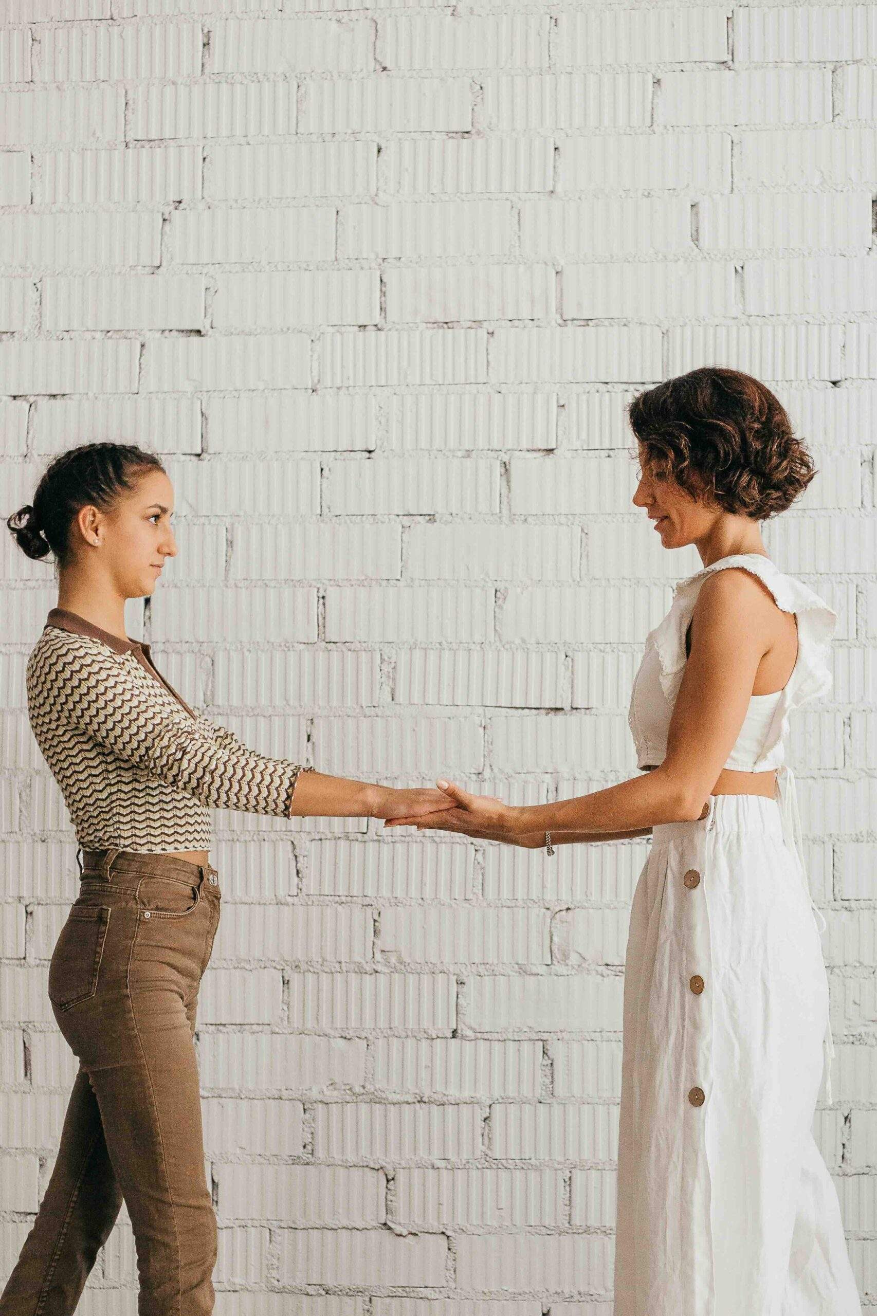 Dos mujeres dándose las manos frente a una pared blanca